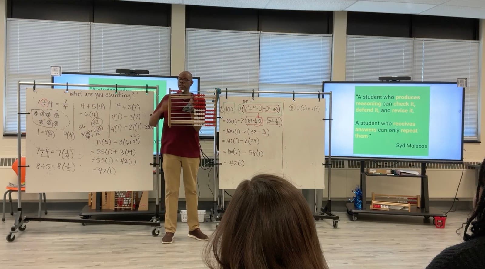 Kevin Moore holds a rekenrek while facilitating, beside a slide reading "A student who produces reasoning can check it, defend it, and revise it. A student who receives answers can only repeat them."